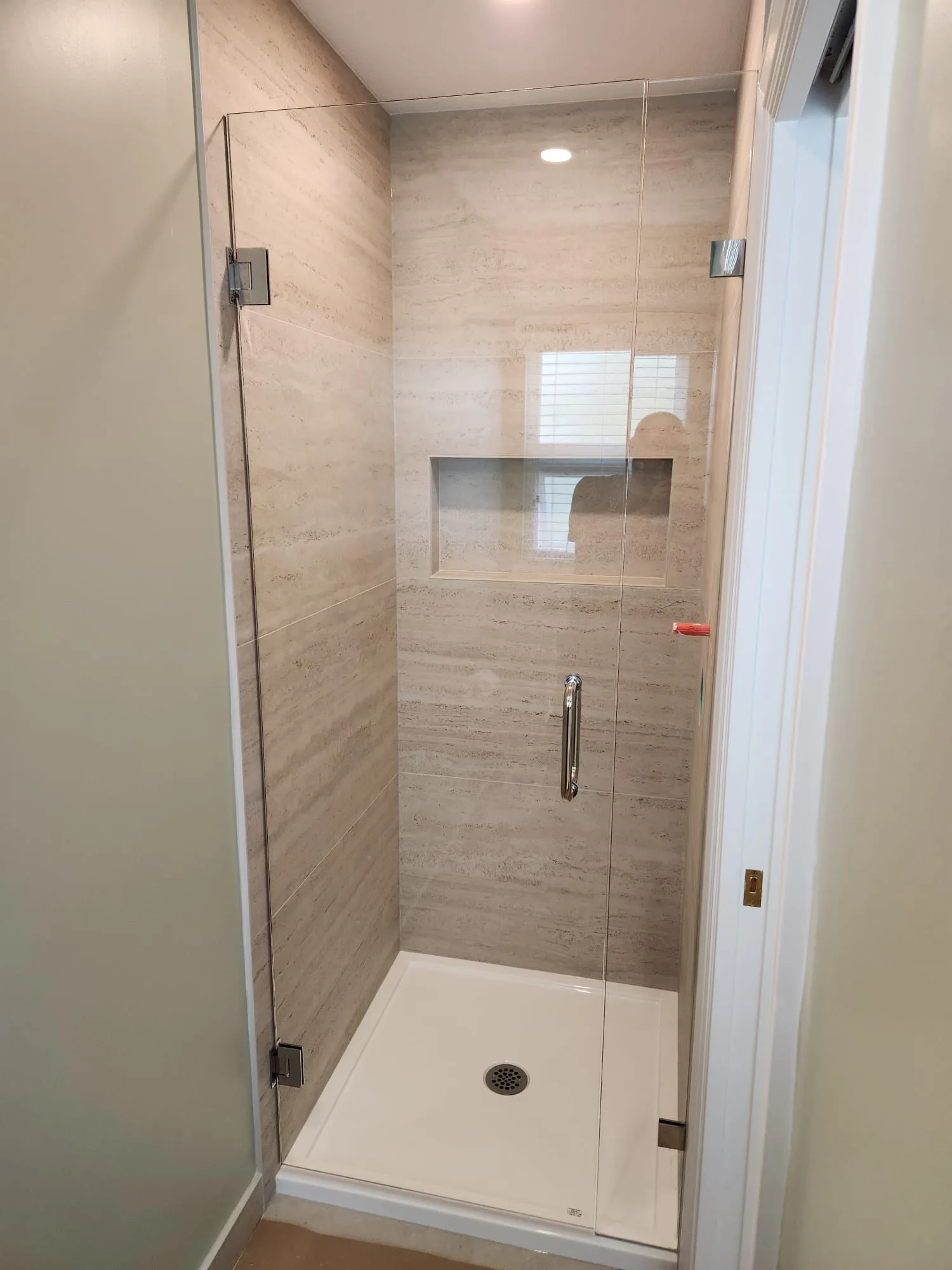 Frameless shower glass in niche opening — angle view showing chrome hinges and tight silicone seal