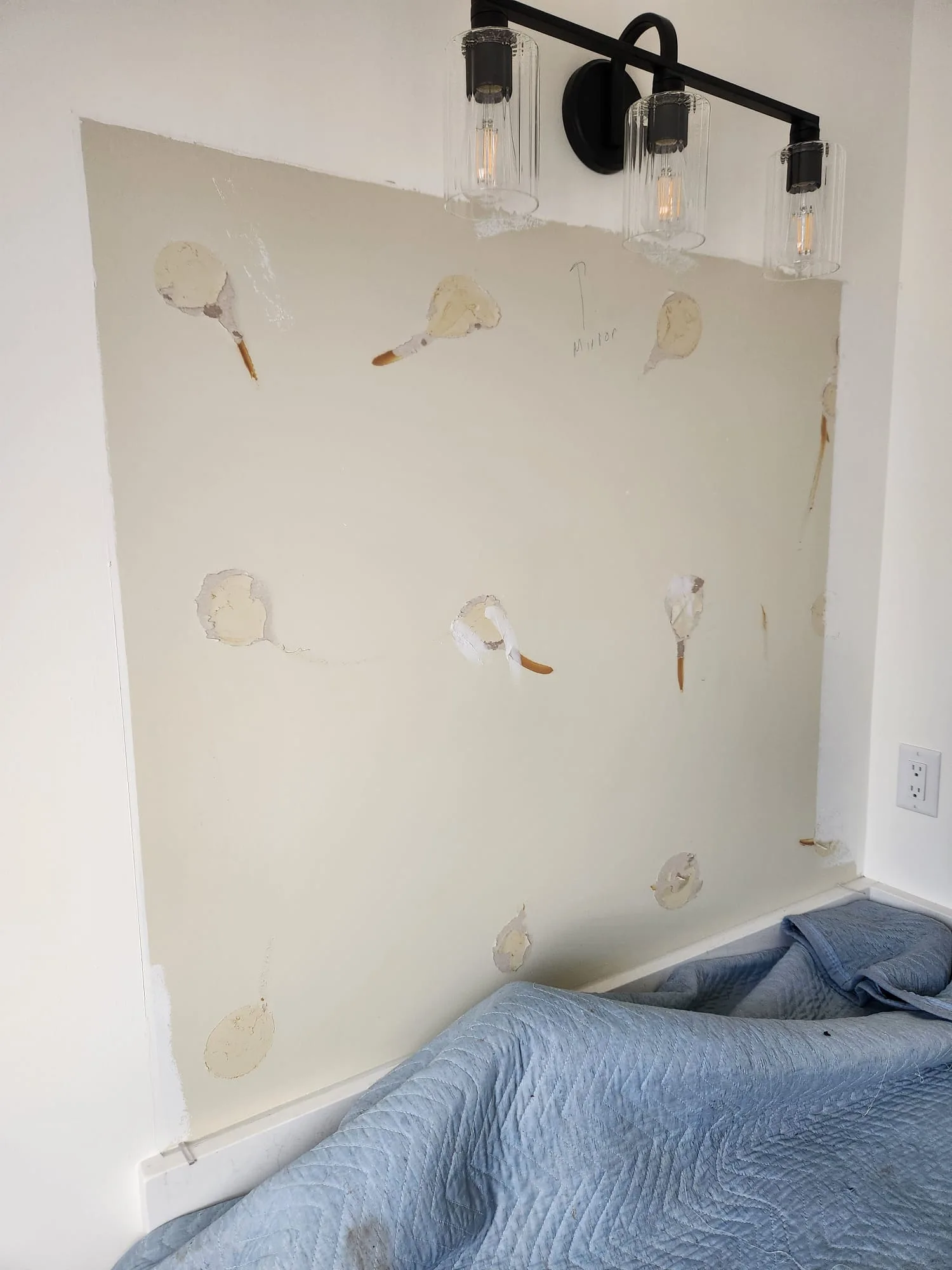 Before installation — wall with mastic adhesive dots where old mirror was removed, matte black vanity light above