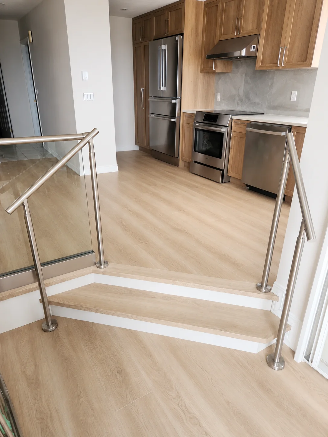 Stainless post handrail system at stair landing with glass panels — open-concept kitchen in background