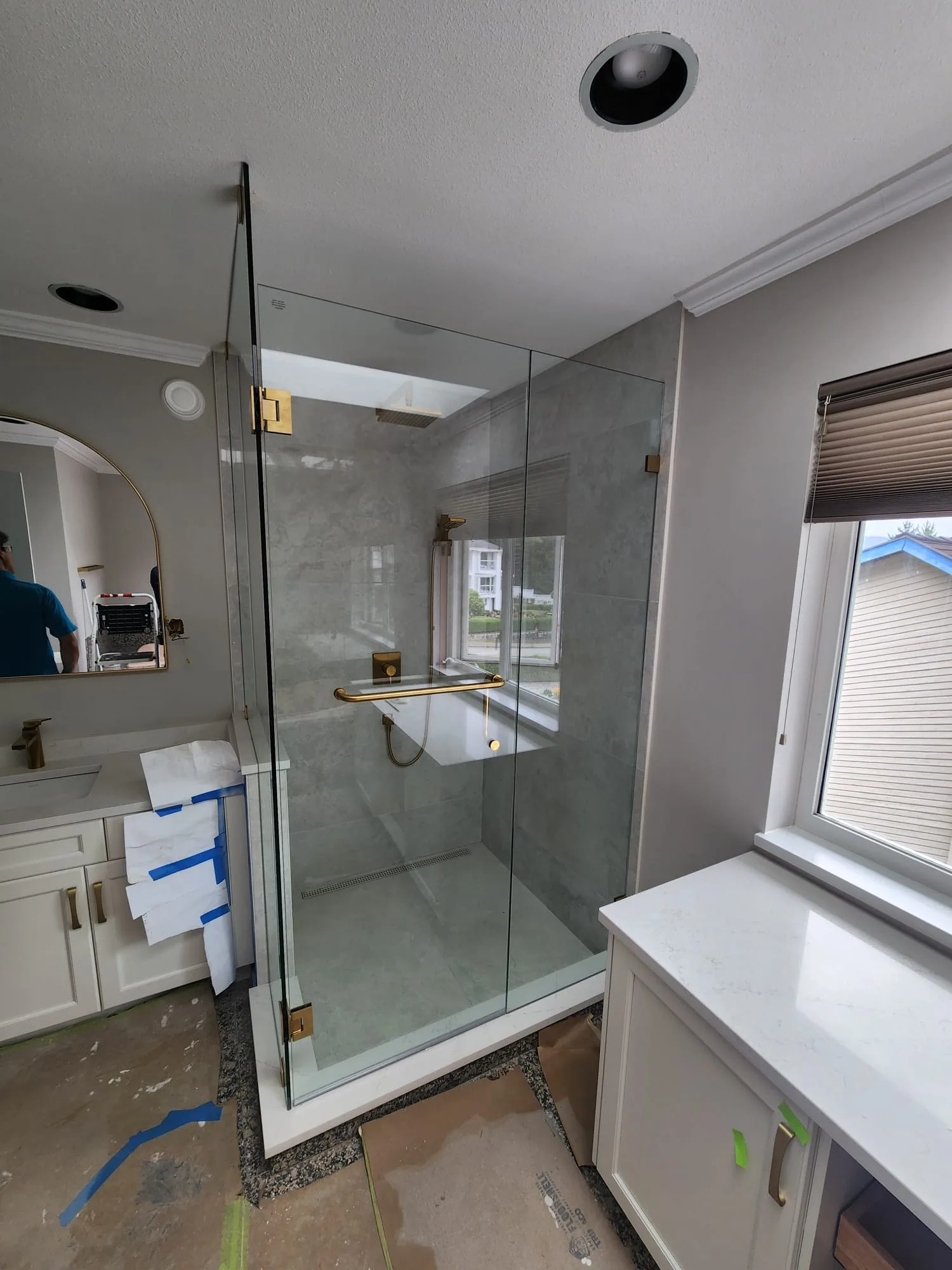 Wide-angle view of completed shower glass installation showing vanity and arched mirror beyond