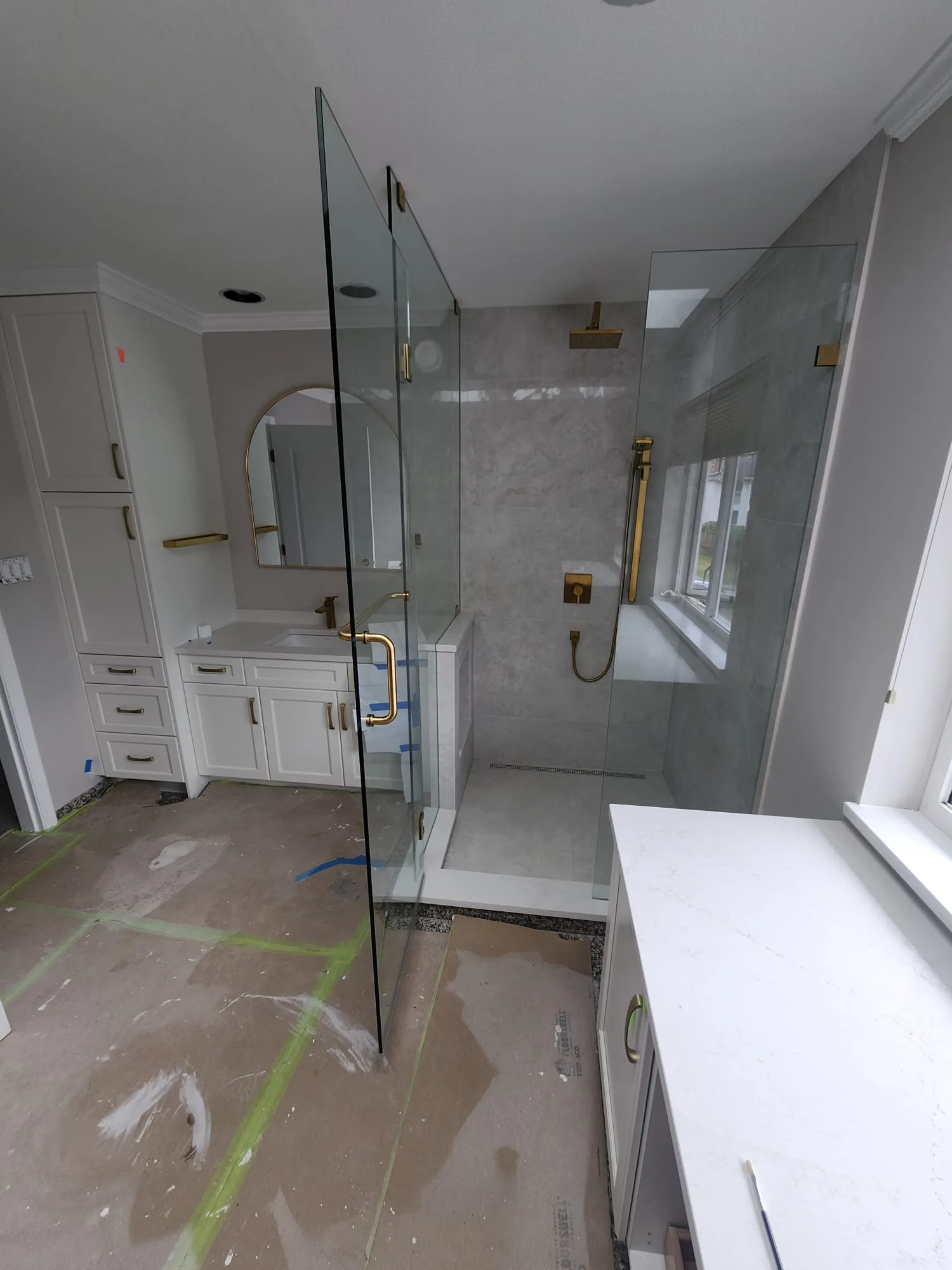 Front view of frameless shower door with brushed gold pull handle and rain head