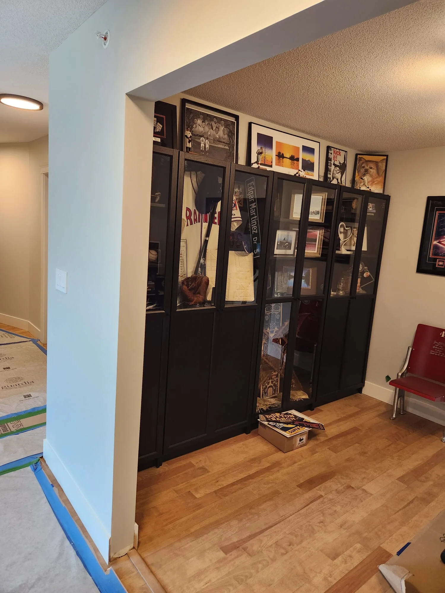 Before installation — bare door opening from hallway with no glass, sports memorabilia display cabinets in den beyond