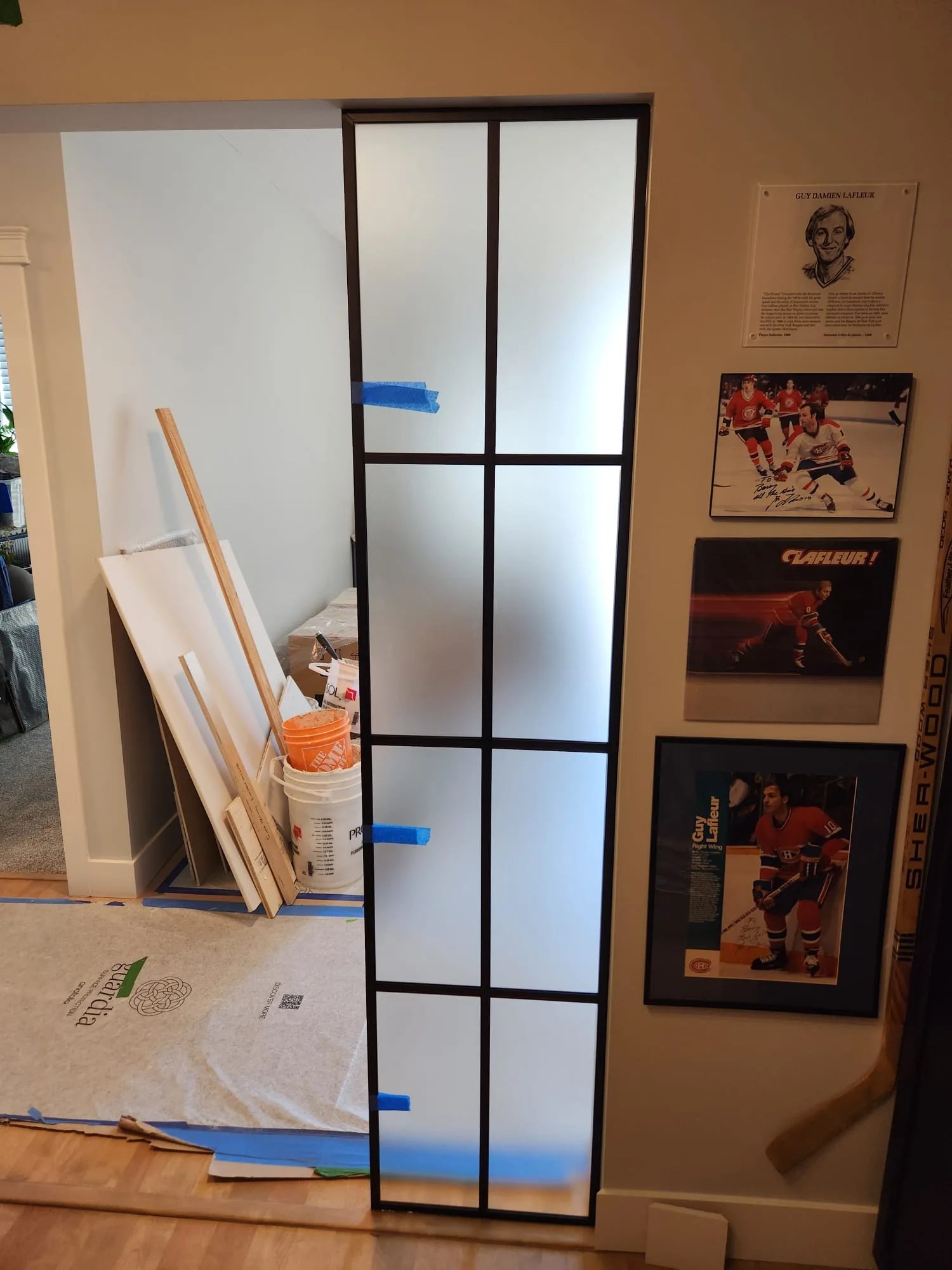 Side lite installation in progress — protective film still on glass giving frosted appearance, Guy Lafleur hockey memorabilia visible on adjacent wall