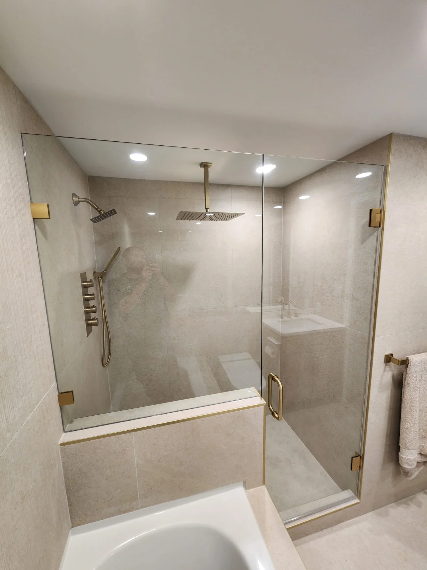 Wide angle of completed shower enclosure — fixed panel, swing door, and return panel with gold towel bar, soaker tub integrated beside