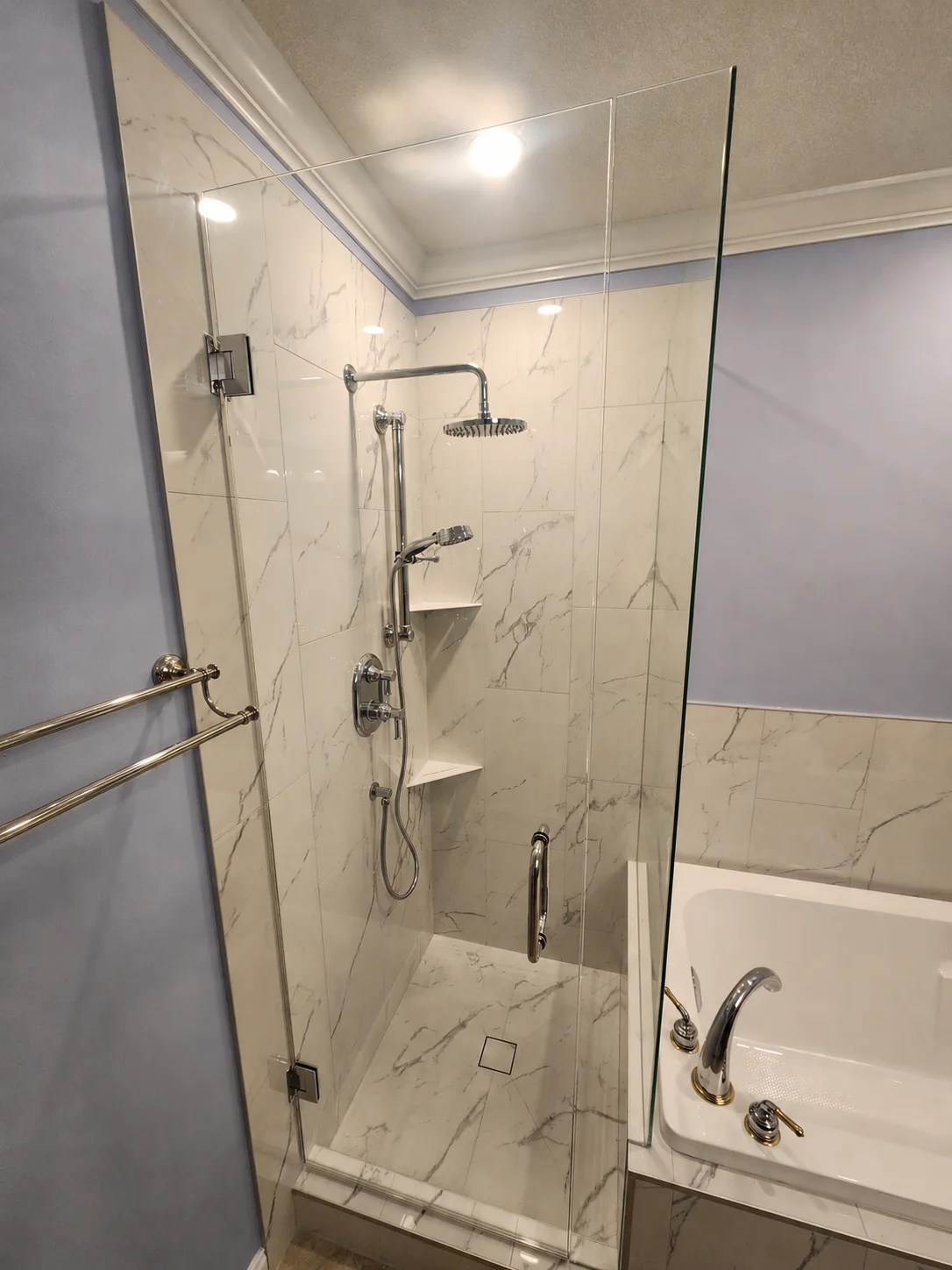 Interior view of frameless shower — chrome rain head, corner shelves, and floor drain visible